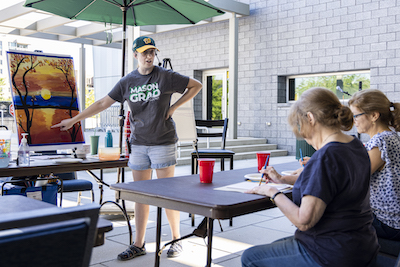 woman in mason gear teaching a painting class outside