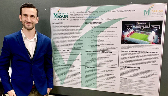 A man in a blue jacket and white shirt stands in front of a poster with information.