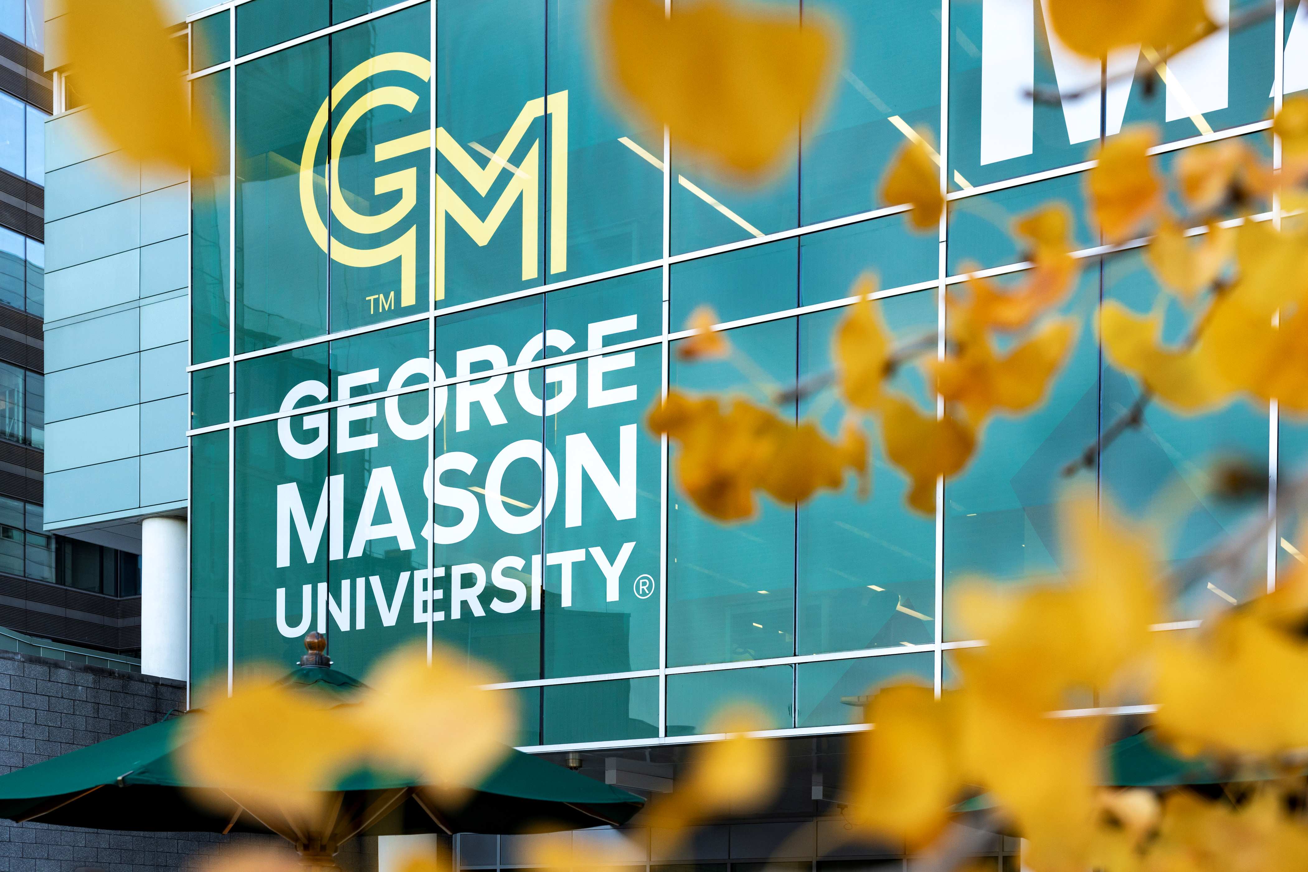 Leaves frame the George Mason logo on the windows of Van Metre Hall