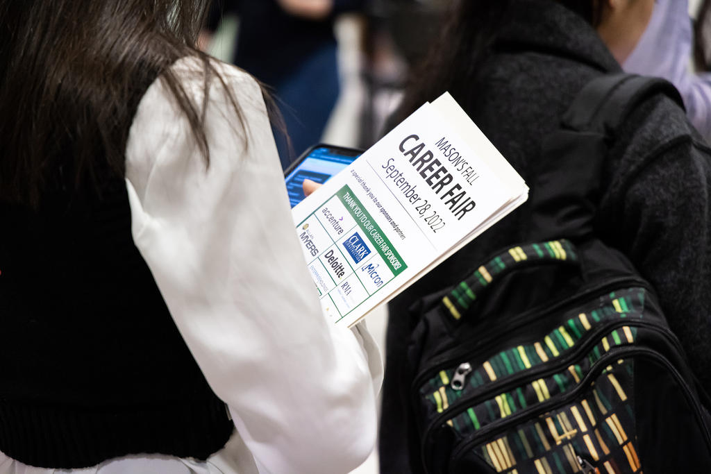 A student holds a career fair information packet in hand amidst a crowd. Their face cannot be seen.