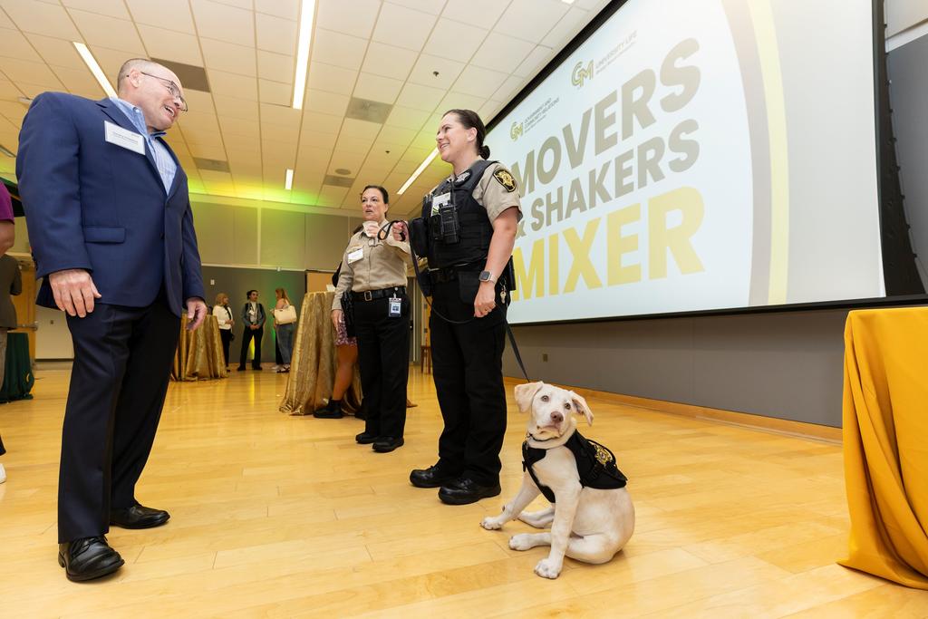 George Mason Police officers have a conversation with a community member at the Movers and Shakers Mixer, with a K9 at their side