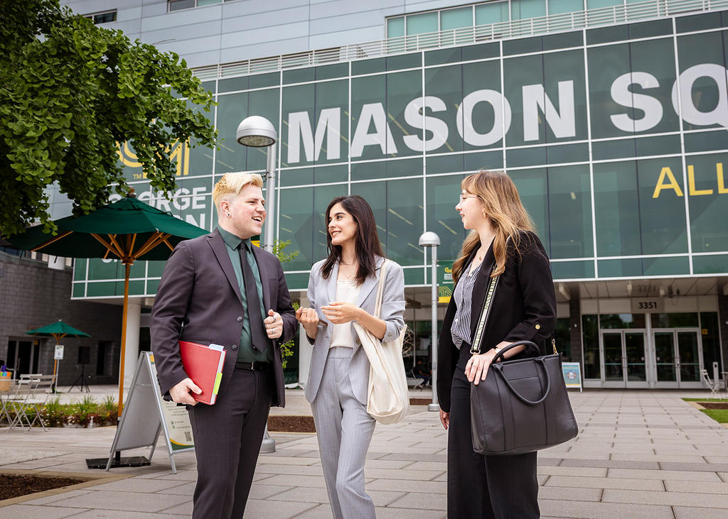 Three students in professional attire stand talking on the Mason Square Plaza.
