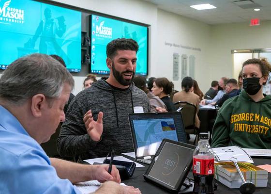 Students and faculty gather around tables to discuss research presentations at the Carter School undergraduate research symposium